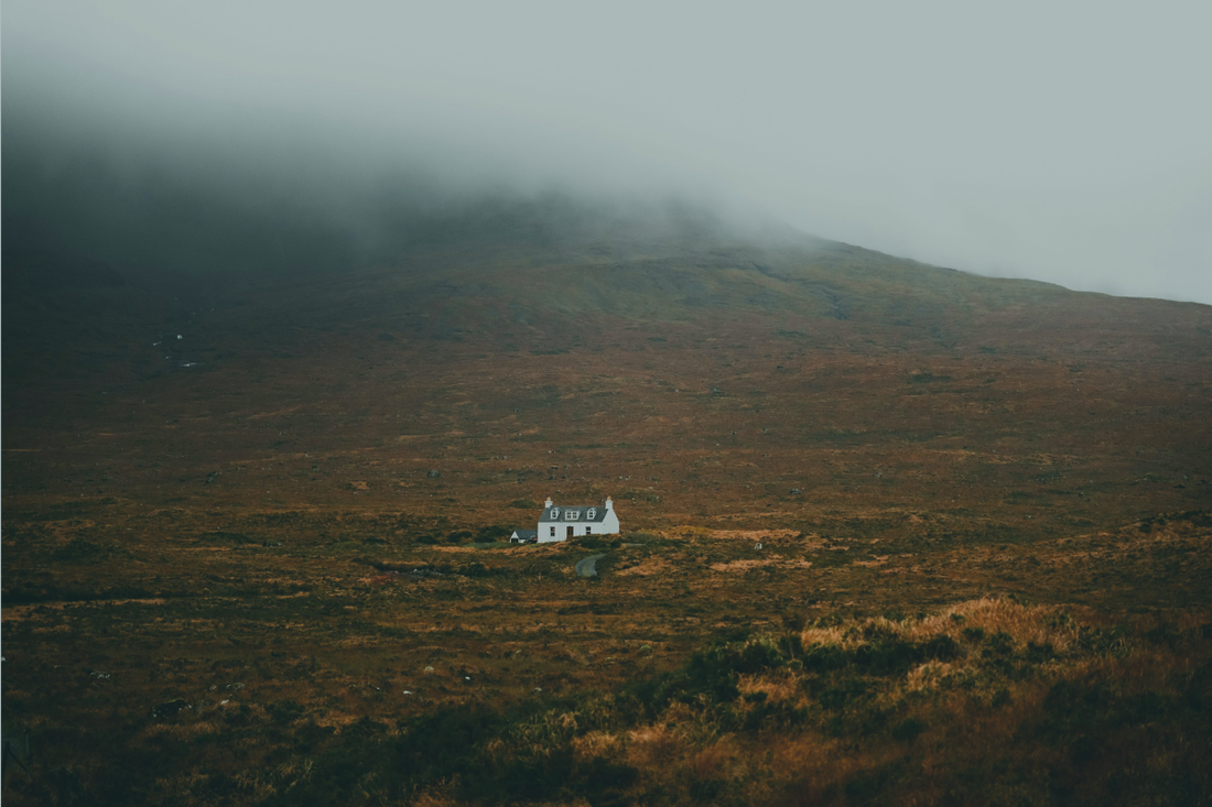 A small white cottage sits alone on a vast brown hillside as low cloud rolls over the ridge above — from a BRÍ Wellness blog post on overthinking, chronic stress, and the connection between sustained mental load and immune resilience.